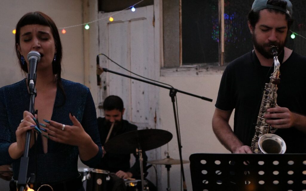 Une photo d'un groupe de musique, avec une femme qui chante, un homme qui joue de la trompette et un autre qui fait de la batterie.